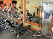Fitness Center With Cardio Equipment Weight Bench, and Weight Machine Facing Large Mirrors With Reflection of Red Stability Ball, Weight Balls, and Towel Station