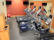 Fitness Center With Cardio Equipment, Weight Bench, and Weight Machine Facing Large Mirrors, Towel Station, Red Stability Ball, and TVs