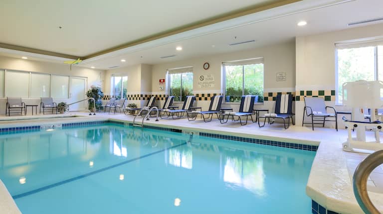 Heated Indoor Pool With Chairs, Loungers, and Outside Views