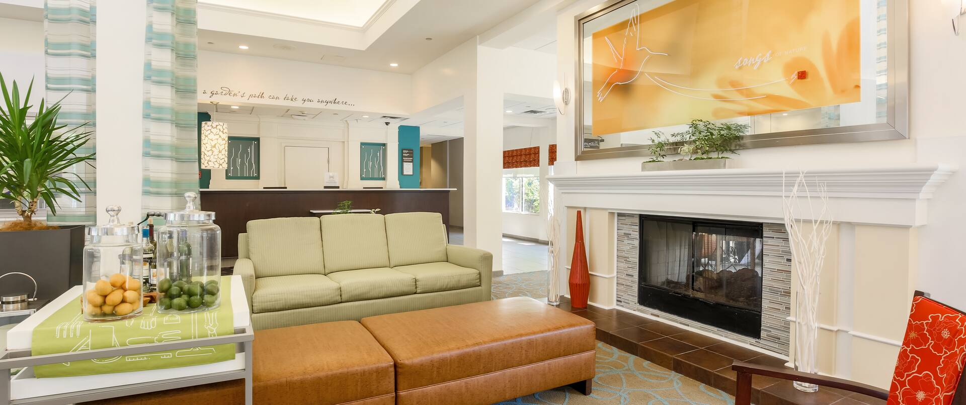Lobby Lounge Area With Art Above Fireplace, Soft Seating, Beverage Station and View of Front Desk in Background