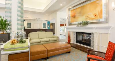 Lobby Lounge Area With Art Above Fireplace, Soft Seating, Beverage Station and View of Front Desk in Background