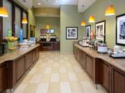 Breakfast serving area with buffet trays, waffle maker, coffee, juice, cereals, oatmeal, fruits, and dining amenities