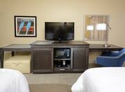 Double queen guestroom with work desk, TV, microwave, and ottoman