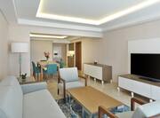 Living Area with Sofa, Coffee Table, Soft Seating Chairs, Cradenza with TV and Dining Table and Kitchen in the Background