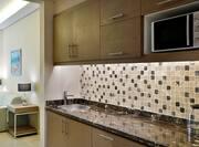 Long Granite Kitchen Counter with Sink and Cabinets along with Microwave in Fully-equipped Kitchen Area in Hotel Suite