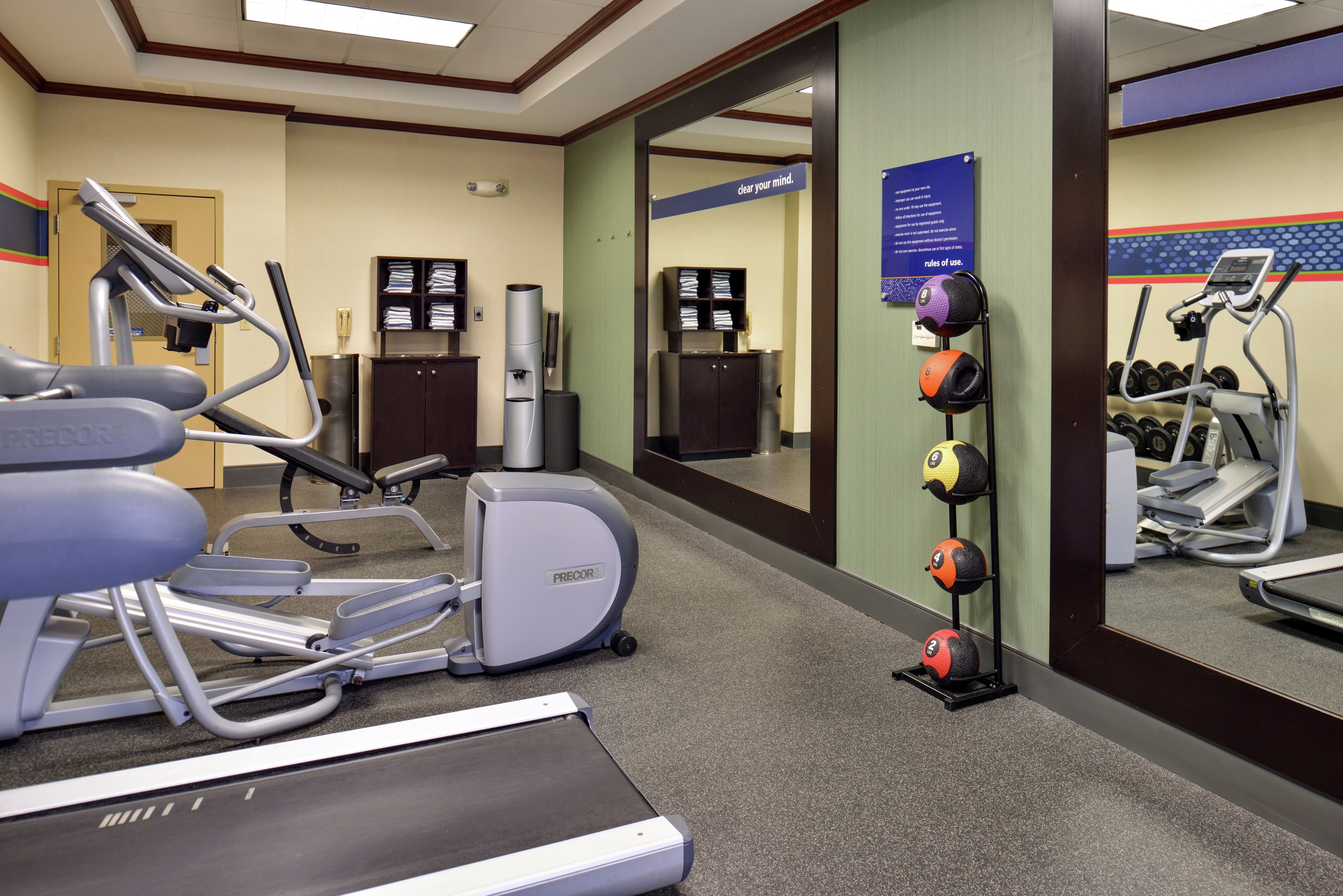 Fitness Center With Cardio Equipment, Towel Station, Water Cooler, and Weight Balls Between Two Large Mirrors