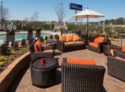 Seating, Tables, and Sun Umbrella on Patio by Pool With View of Hotel Sign in Background