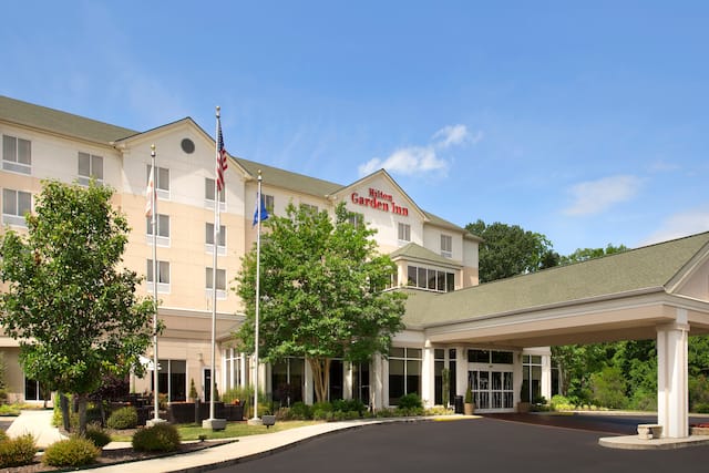 Angled View of Hotel Exterior, Signage, Flagpoles, Landscaping, and Circle Driveway in Daytime