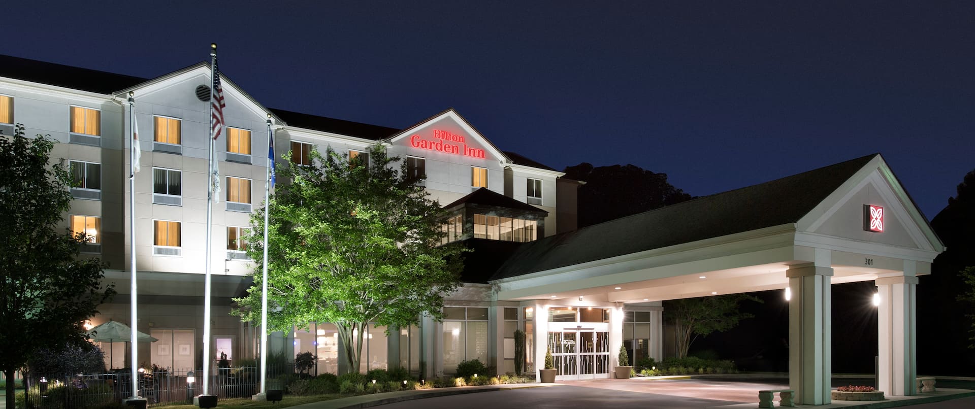  Angled View of Hotel Exterior, Signage, Flagpoles, Landscaping, and Circle Driveway Illuminated at Night