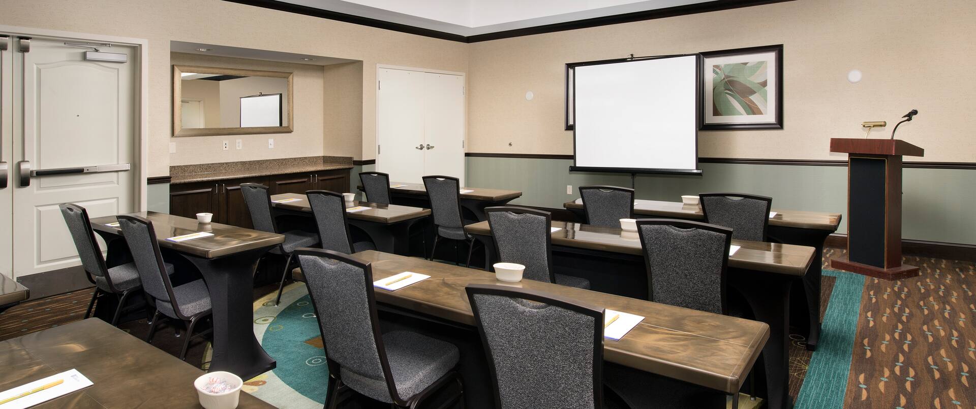 Classroom Style Meeting Room With Tables and Chairs Facing Presentation Screen and Podium