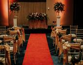 Wedding set-up with chairs either side of red carpeted aisle