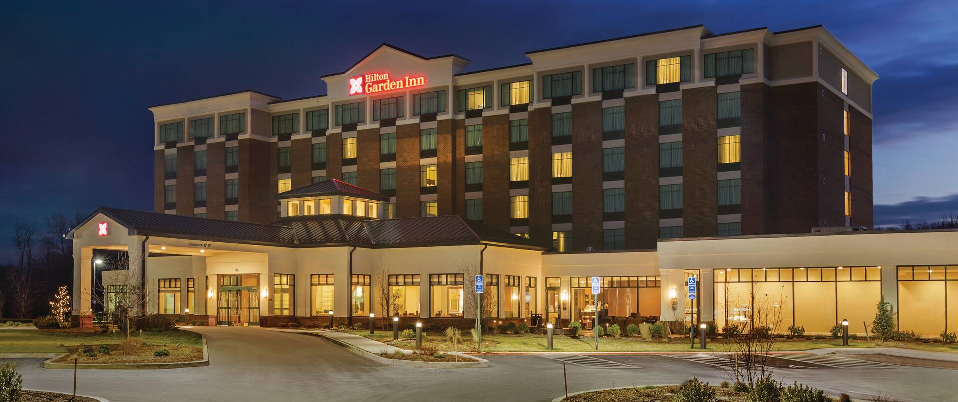 Angled View of Hotel Exterior, Signage, Circle Driveway, Landscaping, and Parking Lot Illuminated at Night