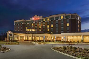 Angled View of Hotel Exterior, Signage, Circle Driveway, Landscaping, and Parking Lot Illuminated at Night