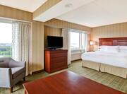 Suite with king bed, work desk, soft chair, TV, and windows with outdoor view