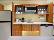 Kitchen With Fridge,  Wood Cabinets With Dinnerware, Coffee Maker, Microwave Over Sink, Dishwasher and Dining Table in King Suite