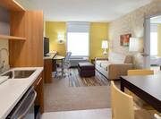 Accessible Suite With Kitchen, Dining Table, TV, Work Desk, Sofa, and Open Doorway to Bedroom
