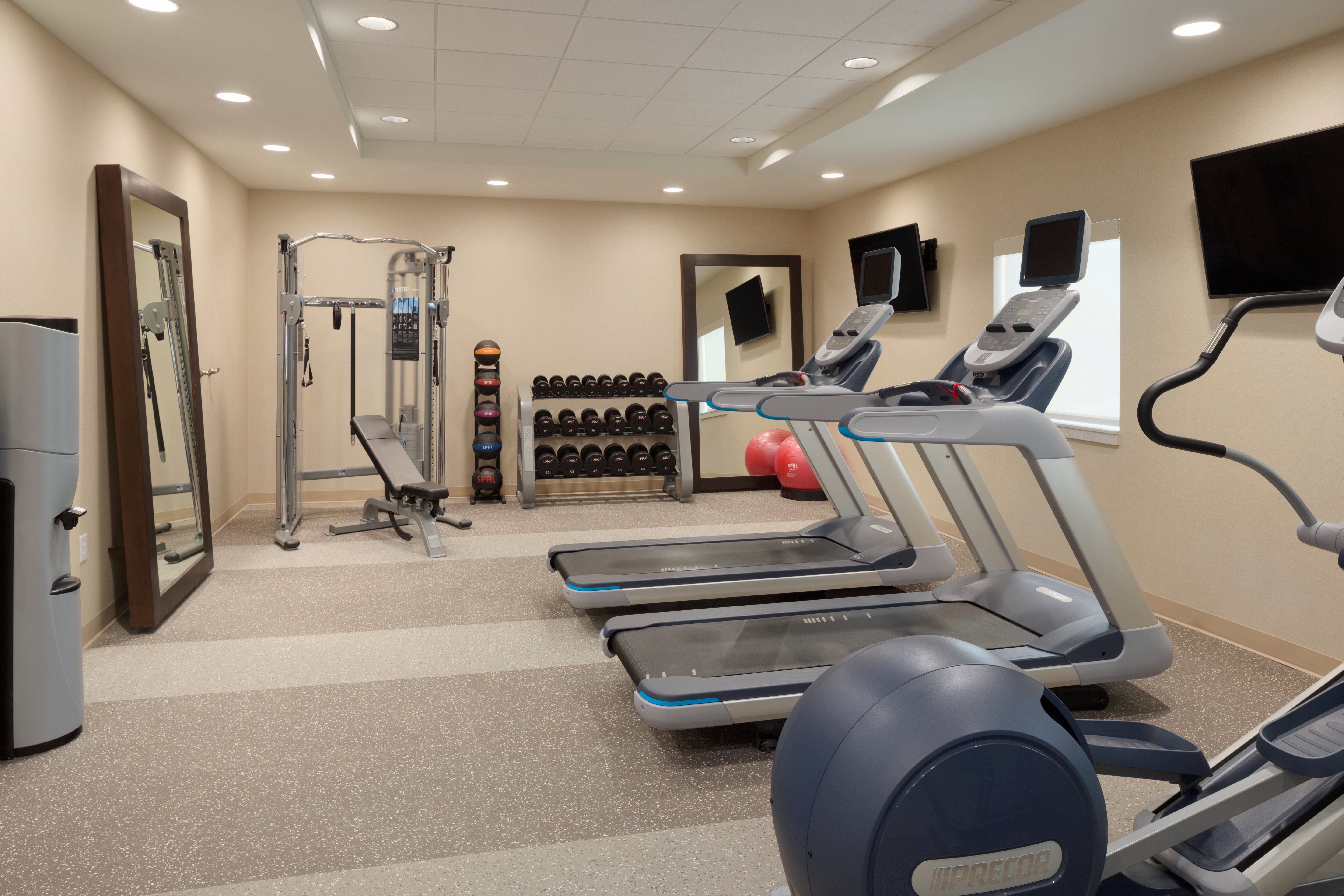 FitFitness Center With Water Cooler, Two Large Mirrors, Weight Machine, Weight Balls, Free Weights, Red Exercise Ball, Two TVs and Cardio Equipment