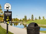 Pet Waste Station Sign, Waste Bag Dispenser, and Black Trash Can in Grassy Pet Area by Water