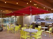 Illuminated Outdoor Patio With Green Chairs, Red Umbrellas Tables, and Three Barbecue Grills at Dusk 