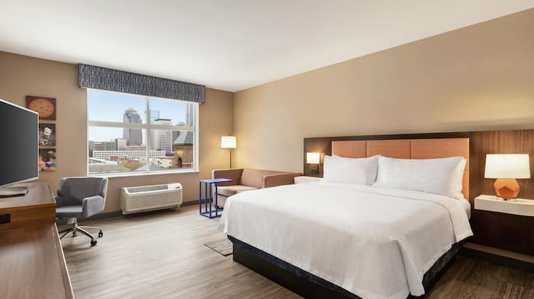 Spacious guestroom featuring TV, comfortable king bed, pull out sofa bed, work desk, and stunning city view.