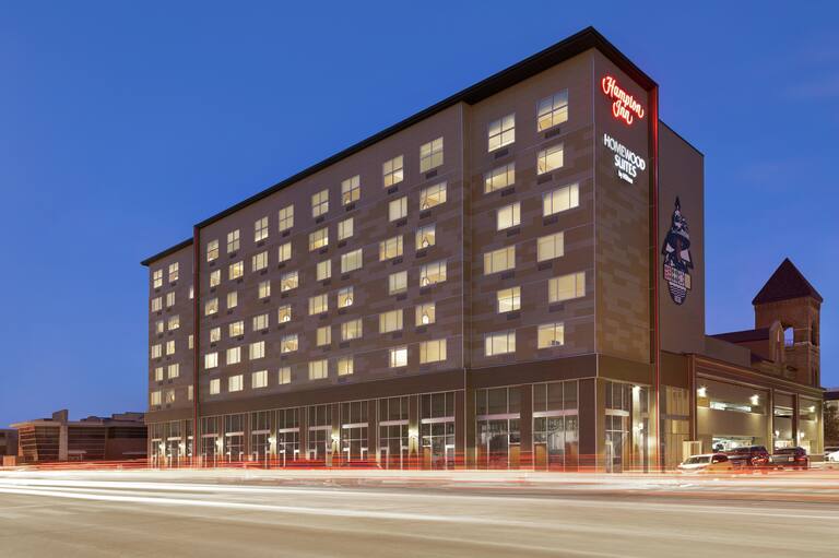 Modern dual property hotel exterior featuring glowing guestroom windows, bell tower, and dusk sky.