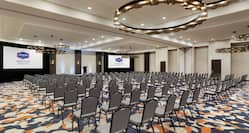 Spacious on-site meeting room featuring theater setup, large projector screens, and podium at front of room.