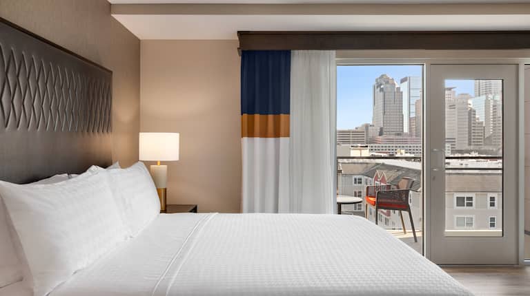 Bright private bedroom in suite featuring comfortable king bed, walk out balcony with seating, and stunning city view