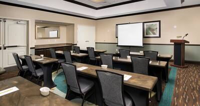Classroom Setup in Meeting Room With Tables and Chairs Facing Presentation Screen, and Podium