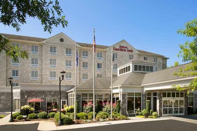 Daytime View of Hotel Exterior With Signage, Flagpoles, Landscaping, and Porte Cochère