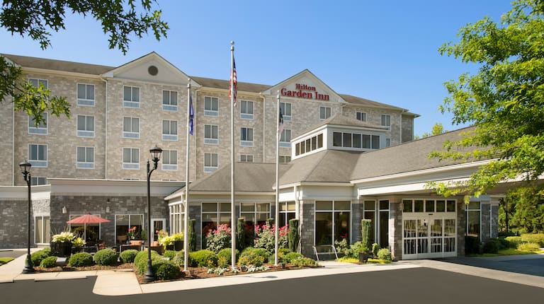 Daytime View of Hotel Exterior With Signage, Flagpoles, Landscaping, and Porte Cochère