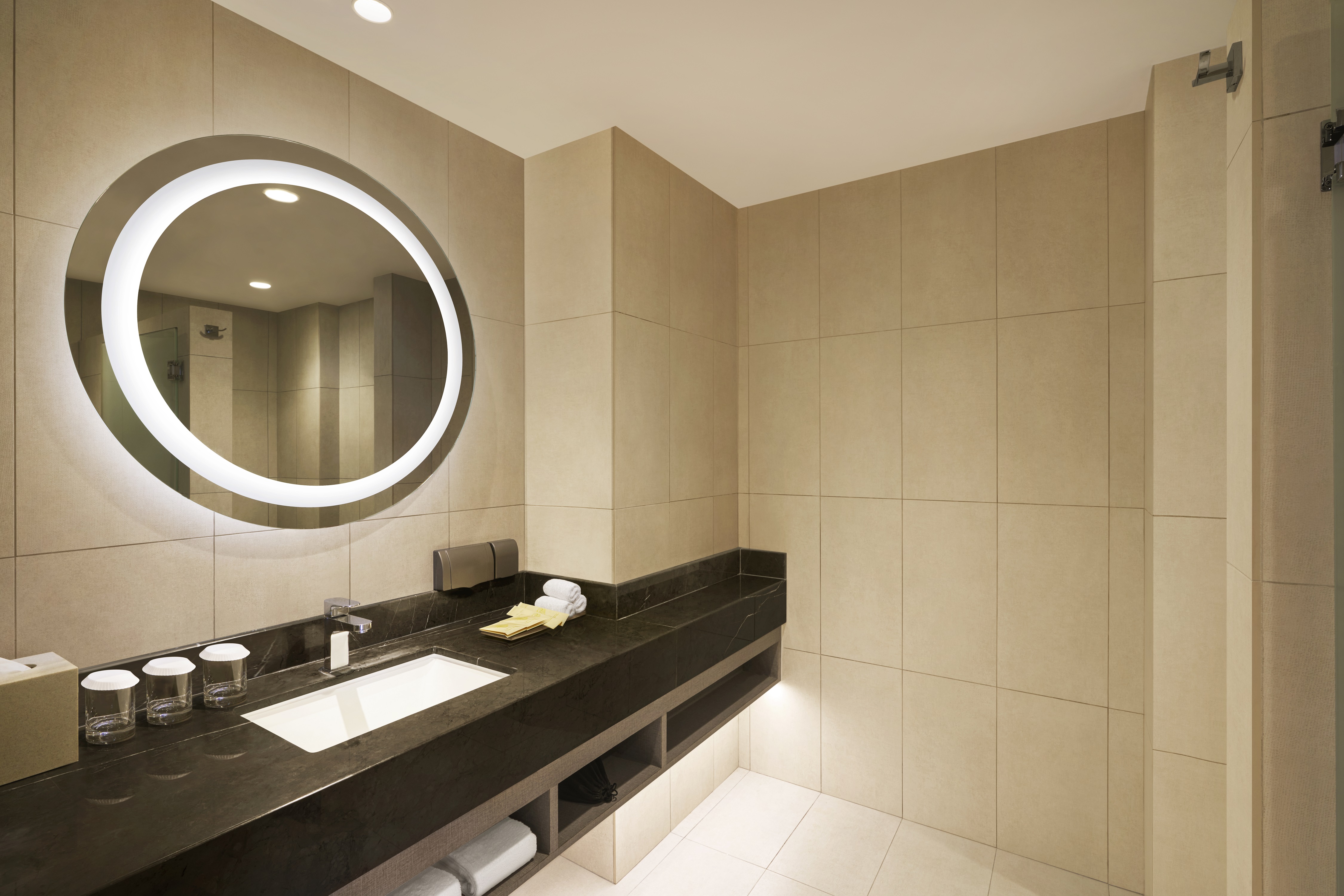 Bathroom Vanity Area with Amenities and a Round Lit Mirror