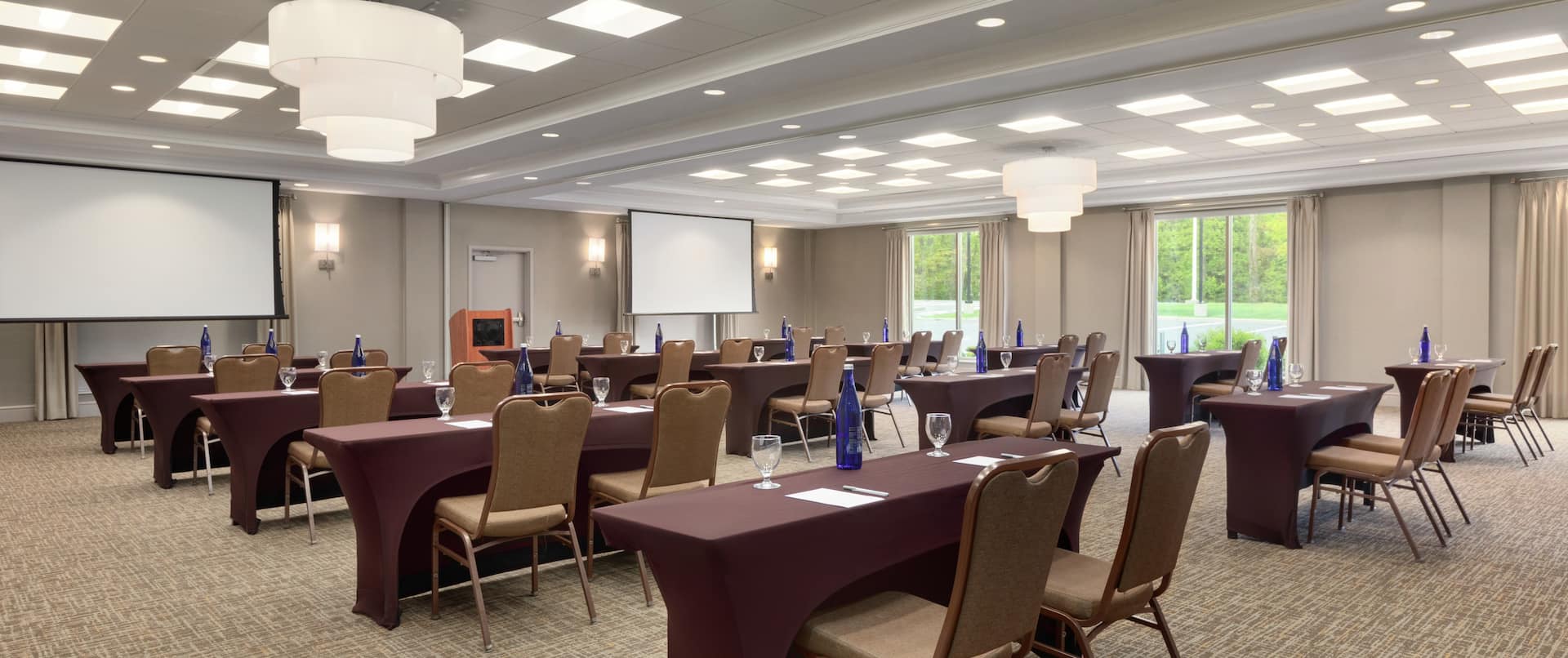 Spacious combined meeting room space featuring classroom style tables, large windows, and dual projector screens at front of room.