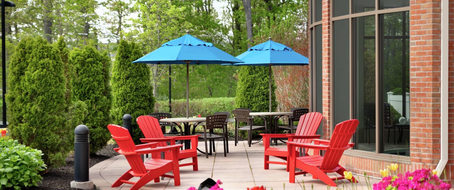 Beautiful outdoor patio area featuring lush trees, ample seating, and view of indoor pool.