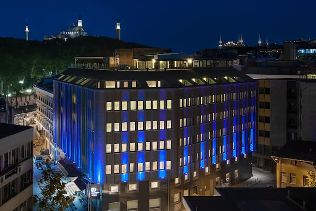 Hotel Exterior Illuminated With Blue Lights, Signage, and City Skyline at Night