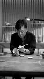 Mies pitää sivellintä kädessään ja esittää Kintsugia teekupilla