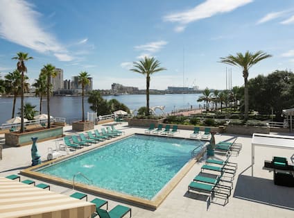 Outdoor pool with lounge chairs, palm trees, and ocean in background