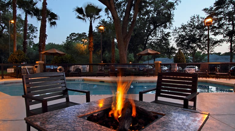 Illuminated Outdoor Area With Fire Pit and Soft Seating With View of Pool  at Night