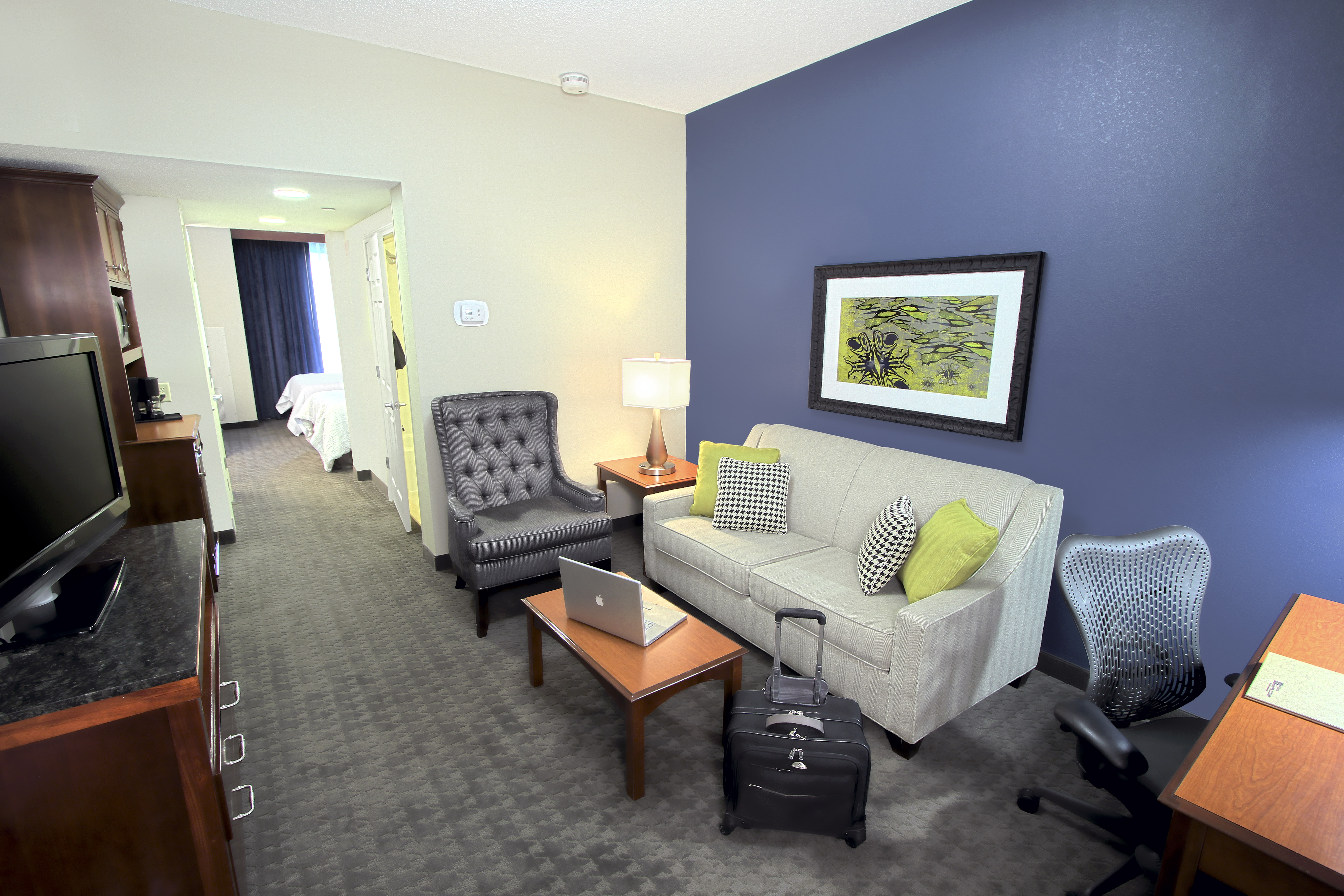 Suite Living Area With Soft Seating, Work Desk, TV, Hospitality Center, and View into Bedroom
