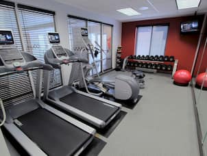 Fitness Center With Cardio Equipment Facing Windows, Weight Balls, Bench, Free Weights, TV, and Red Stability Ball by Mirrored Wall
