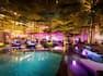 Outdoor bar and lounge after dark with soft purple lights illuminating the table seating and poolside lounging areas