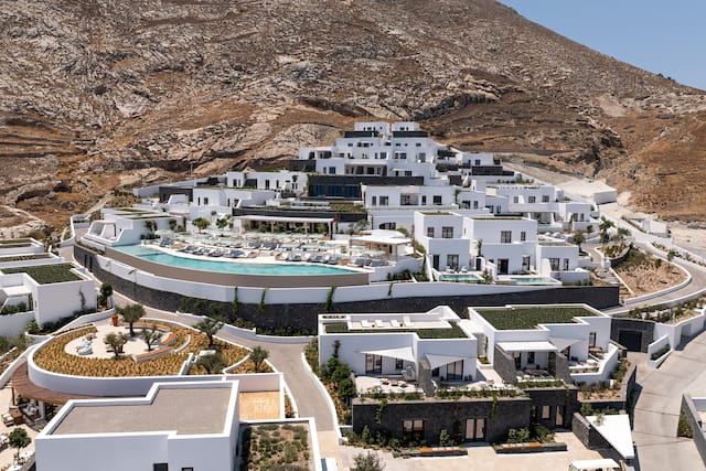 Außenansicht des Gebäudes tagsüber mit weiß gewaschenen Wänden und einem Außenpool mit einer großen Anzahl an Sitzbereichen im Freien.