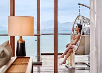 A smiling woman sitting on a hanging chair with views of the ocean in the background