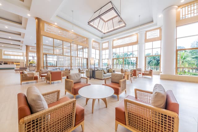 Hotel lobby area with soft seating around tables, as well as a view of palm trees through the window and pillars