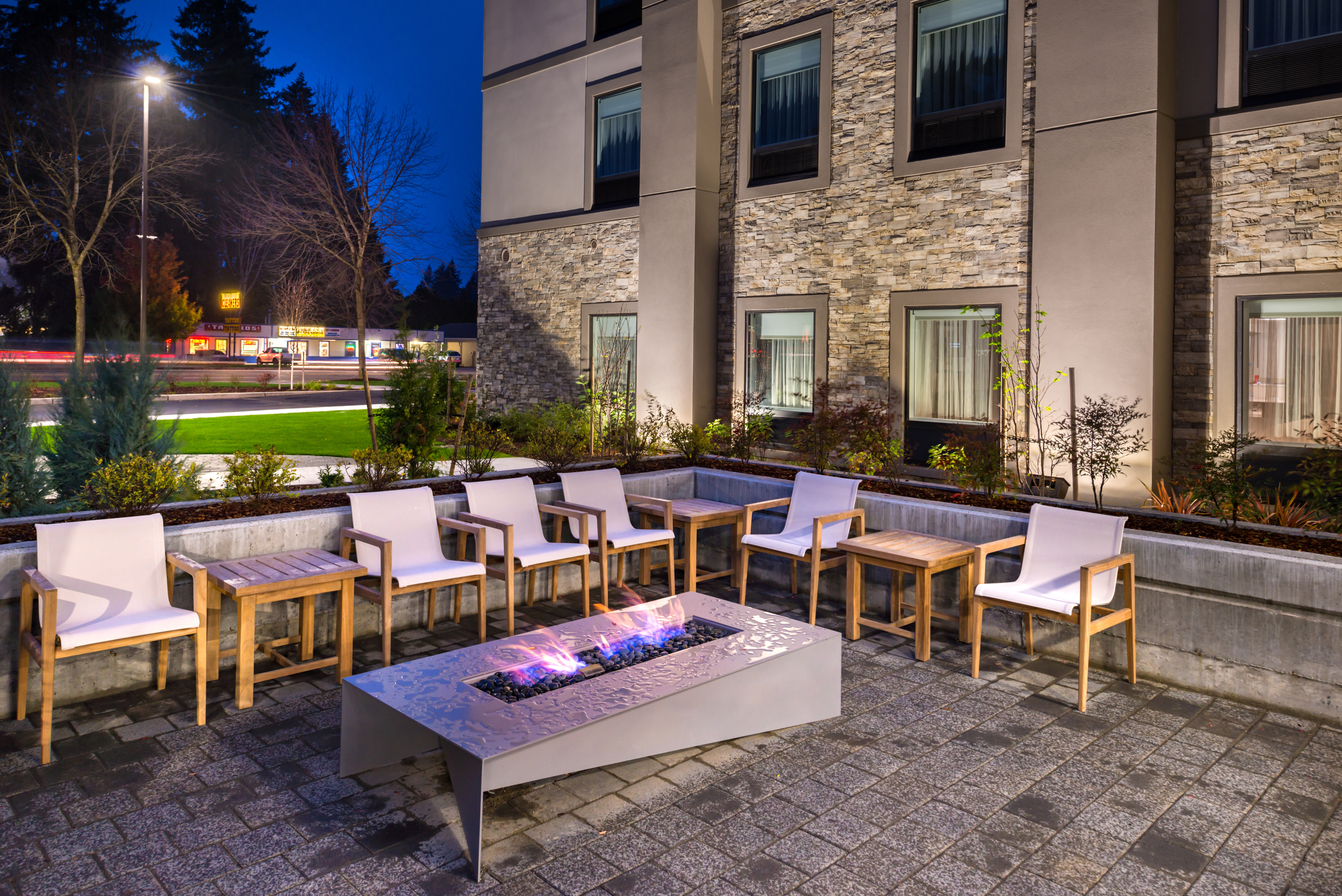 Tables and Chairs Around Fire Pit on Patio and Illuminated Hotel Exterior at Night