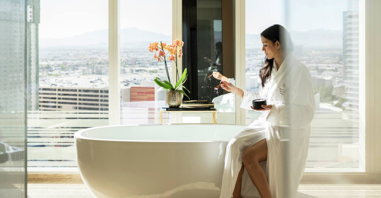 Suite with Woman Sitting on the Edge of a Stand-Alone Tub with Outside View