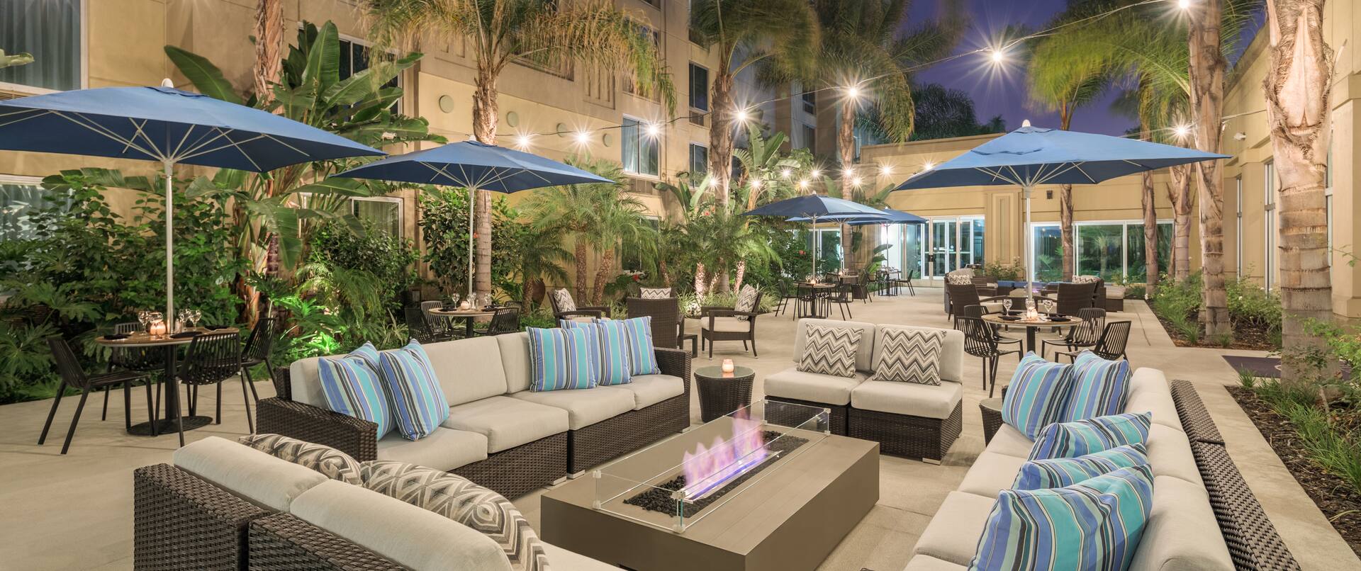 Exterior Courtyard seating area at night with dining tables, chairs, table umbrellas, lounge sofas, and palm trees