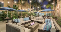 Exterior Courtyard seating area at night with dining tables, chairs, table umbrellas, lounge sofas, and palm trees