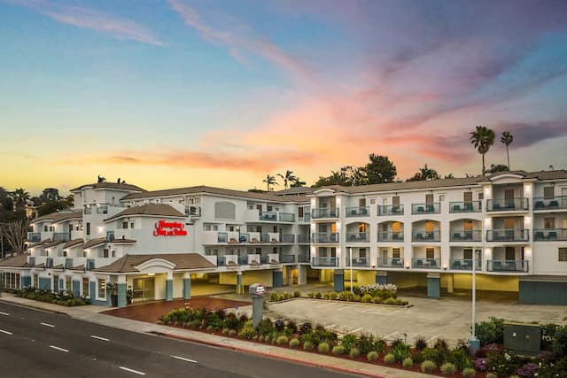 Three-story hotel exterior at dusk, with covered parking and private balconies for rooms.
