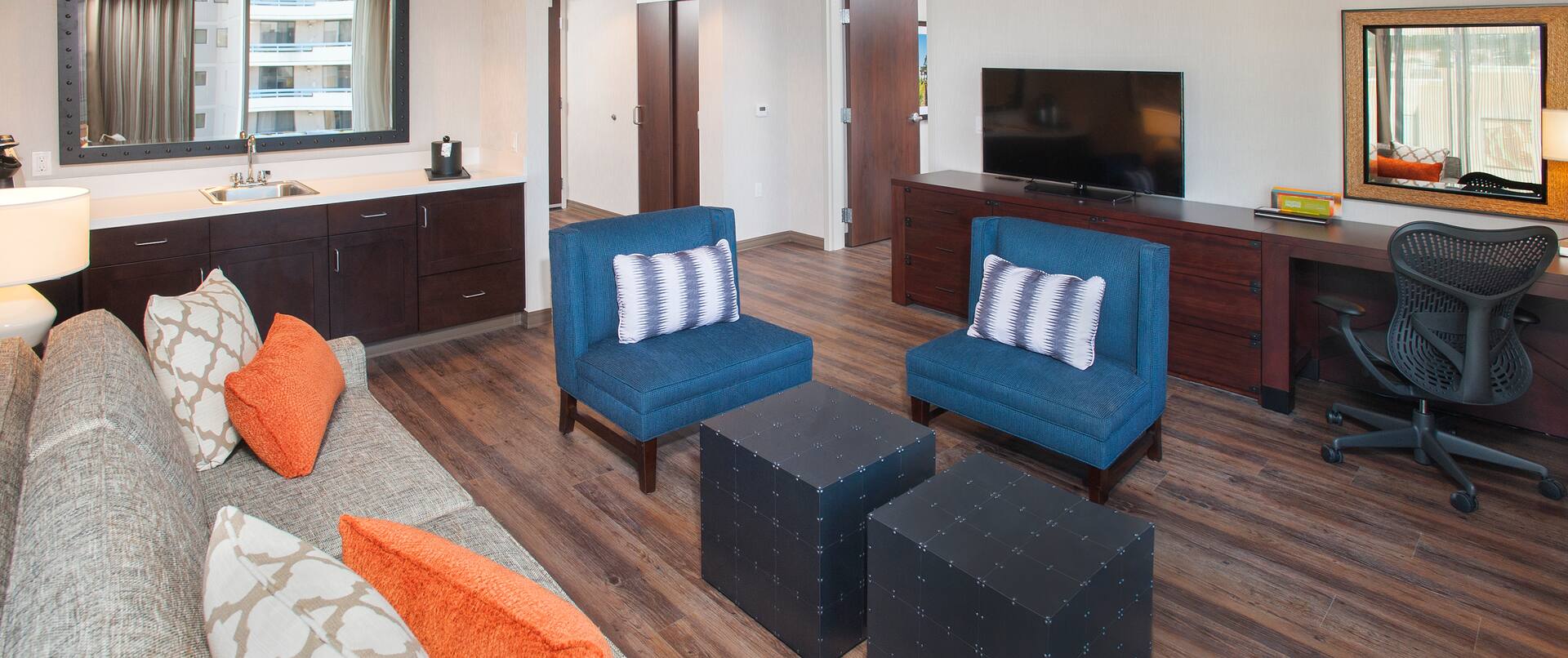 Living Area of 1 Bedroom Suite with Sofa, Chairs, Wet Bar, Open Doorway to Bedroom, TV, and Work Desk