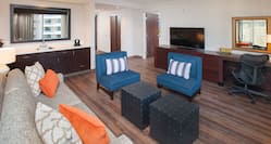 Living Area of 1 Bedroom Suite with Sofa, Chairs, Wet Bar, Open Doorway to Bedroom, TV, and Work Desk